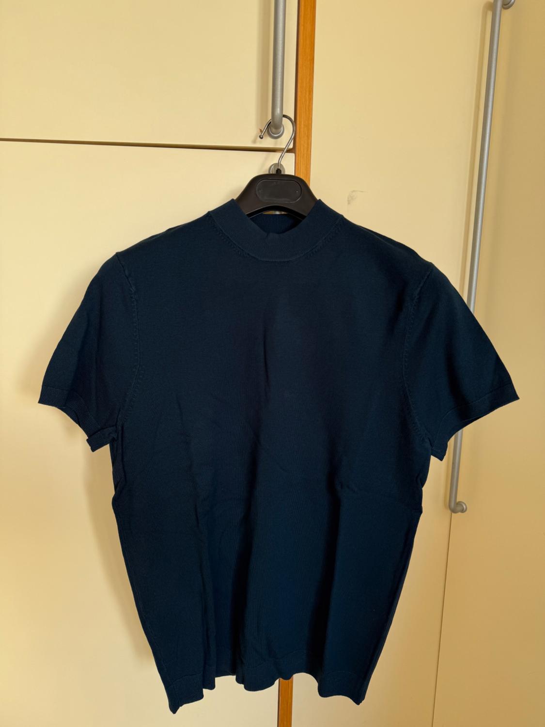 Black short-sleeved t-shirt hanging on a black hanger, against a beige wardrobe background with metallic handles.