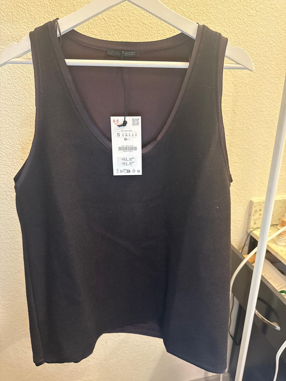 Black sleeveless top hanging on a white hanger, with a visible label showing size S and a price of US$ 4.95. Beige background.