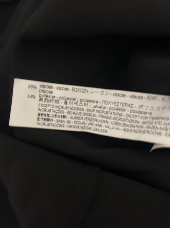 Fabric label on black garment, showing composition: 56% viscose, 44% polyester, with text in various languages.