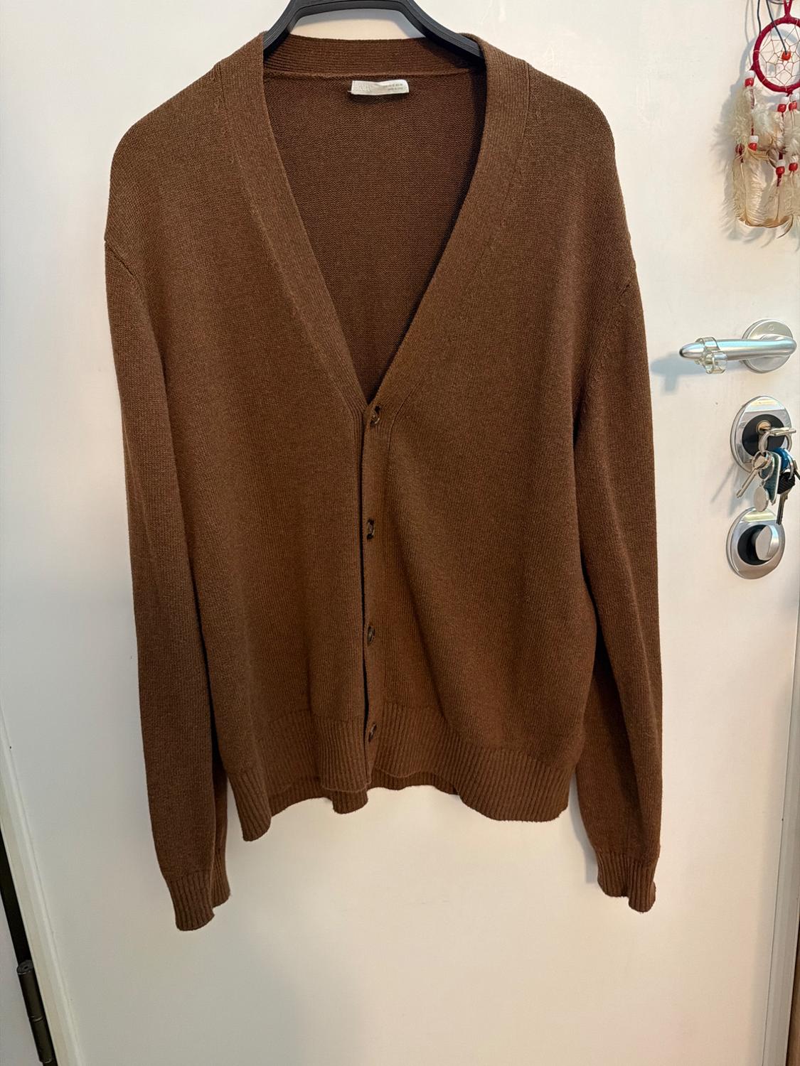 Brown knitted cardigan with a V-neck and buttons, hanging on a white door with keys. Casual and relaxed atmosphere.
