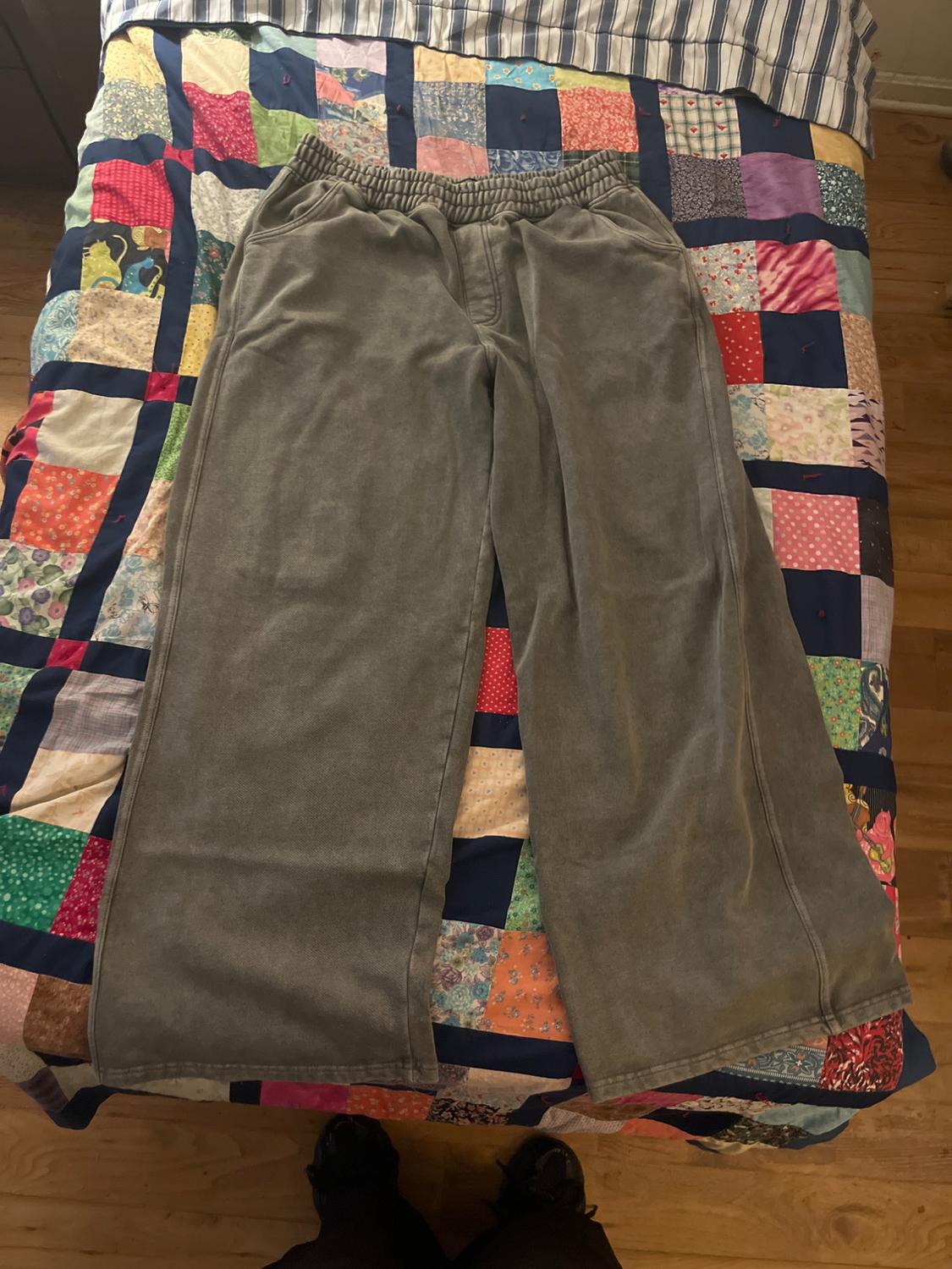 Soft grey fabric trousers on a colourful patchwork quilt on a bed, with wooden flooring visible.