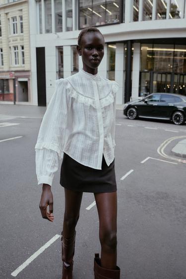 Set aus weißer Bluse mit Rüschen und Stickereien, Rundhalsausschnitt und langen Ärmeln, und schwarzem Minirock.