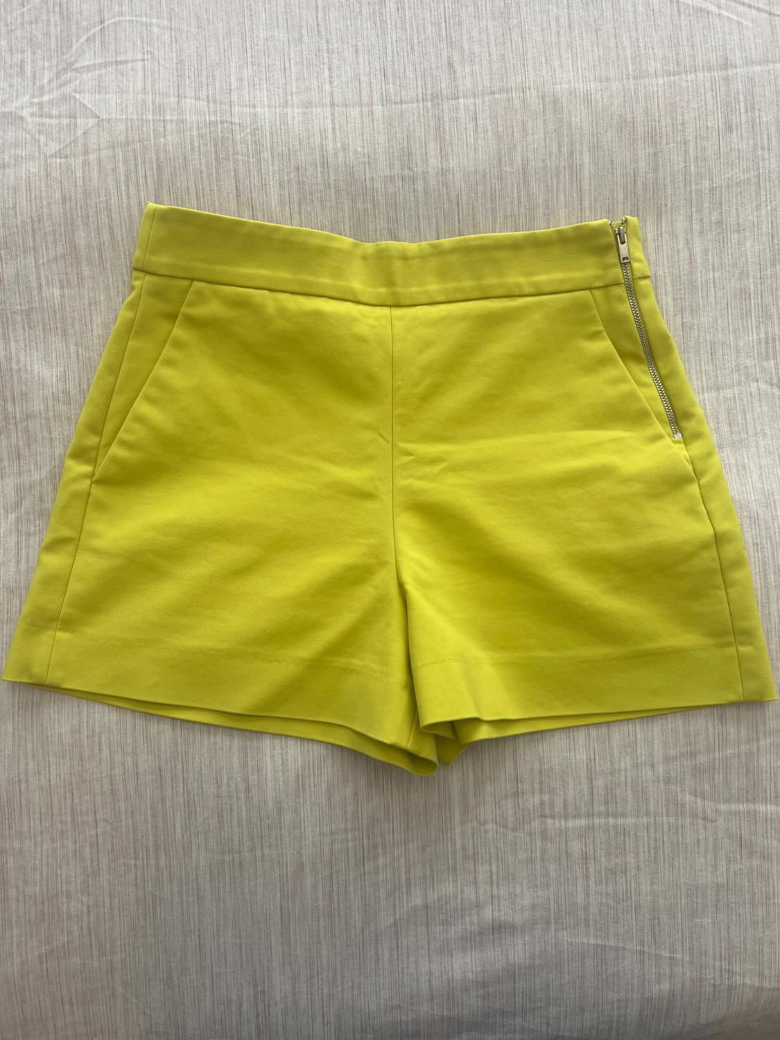 Yellow shorts with a side zip on a light fabric surface with a fine line texture.
