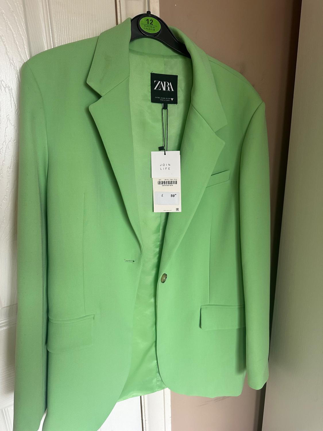 Green jacket hanging on a black hanger with a Zara tag and a price of £59. White door in the background.