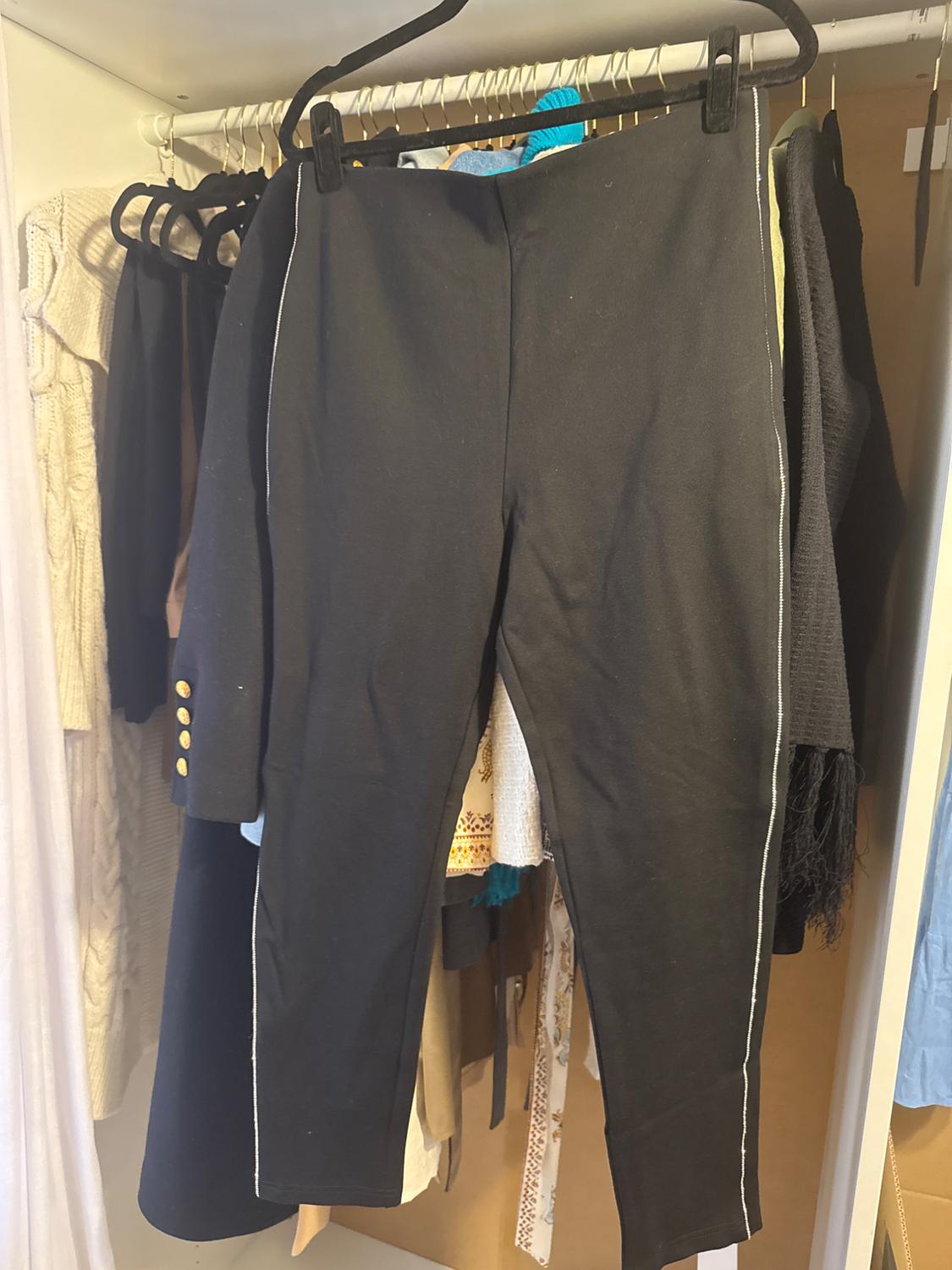 Black trousers hanging in a wardrobe next to various items of clothing, including a coat with gold buttons and jumpers of different colours.