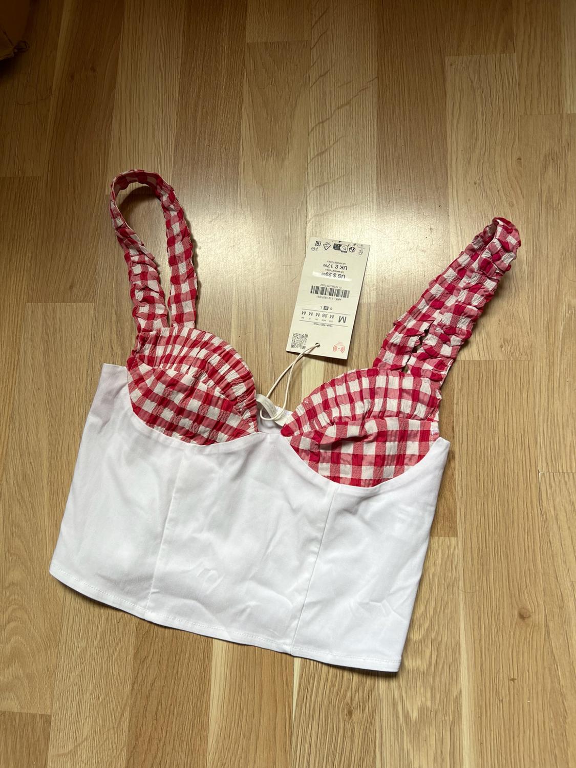 White top with cups and gathered straps, featuring a red-and-white check pattern, on wood. Price tag: US$29.90 UK£17.99.