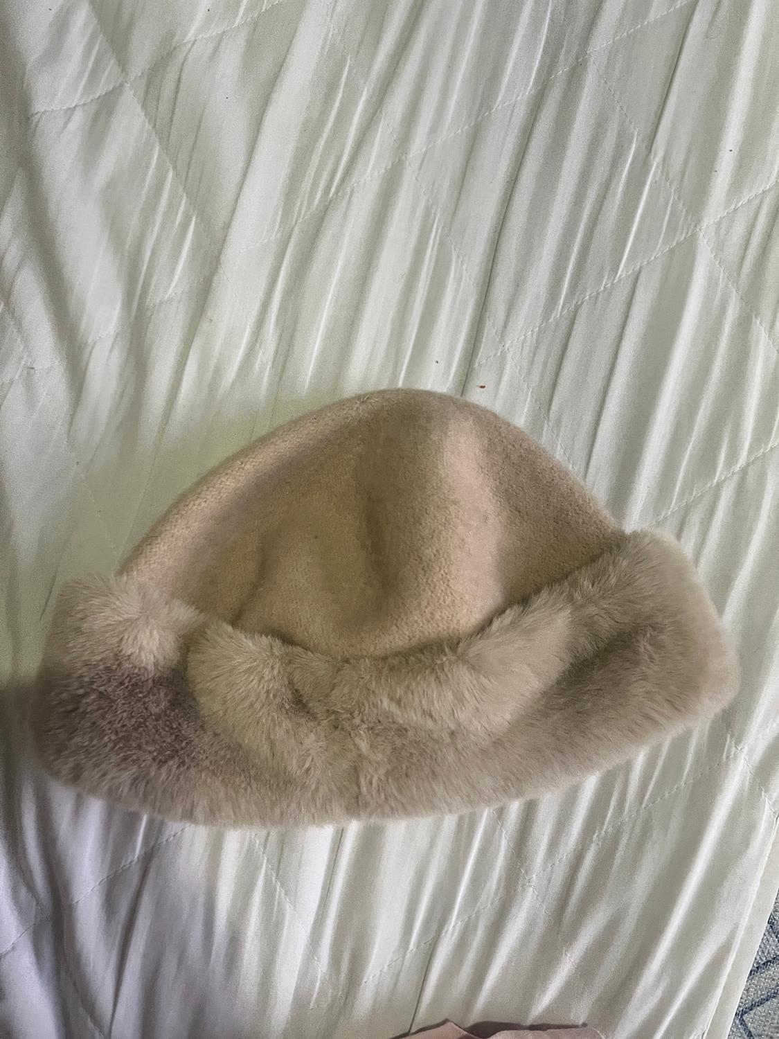 Beige hat with a fluffy brim on a white quilted bedspread.