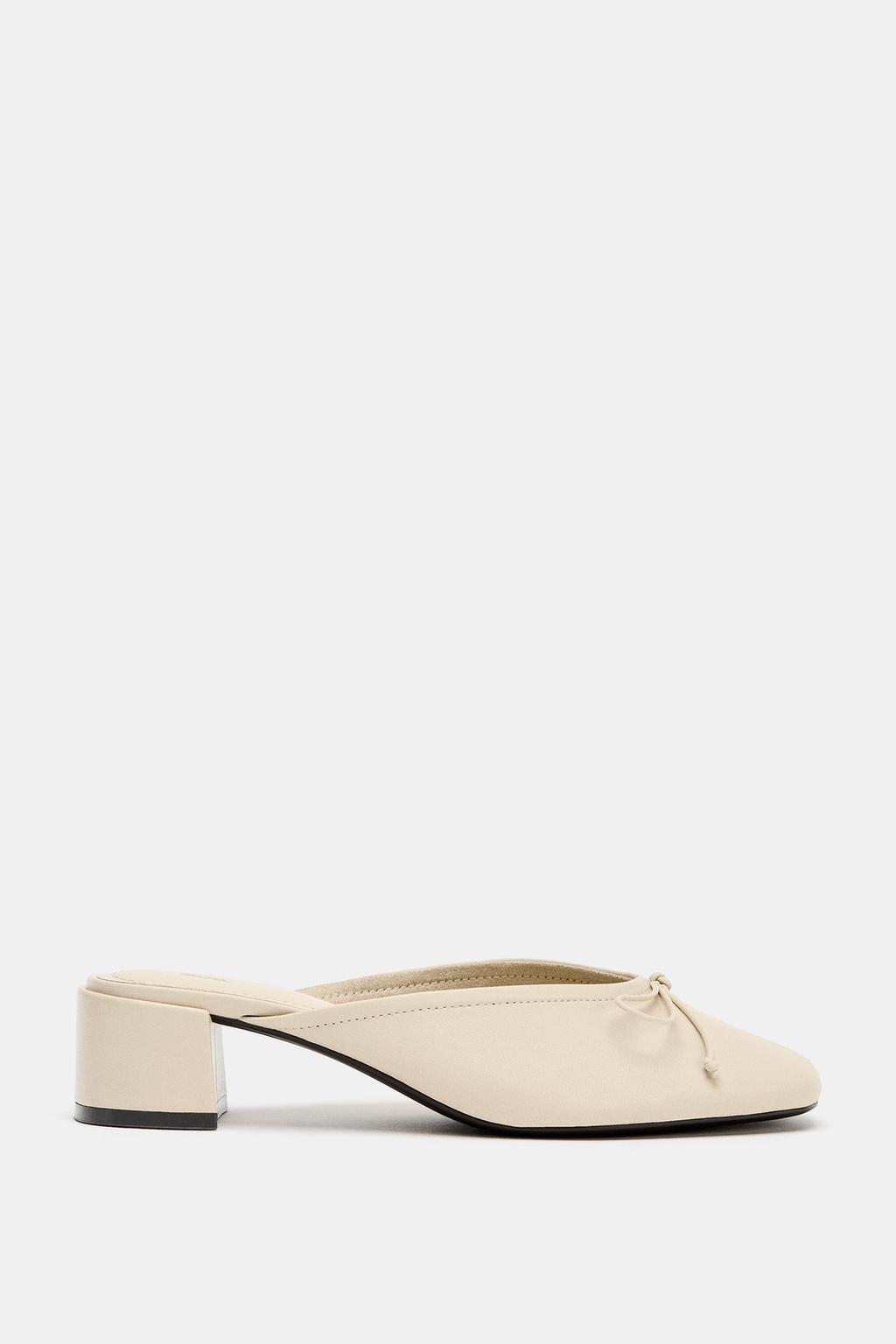 Side view of a beige shoe with a low heel and a bow detail on the top.