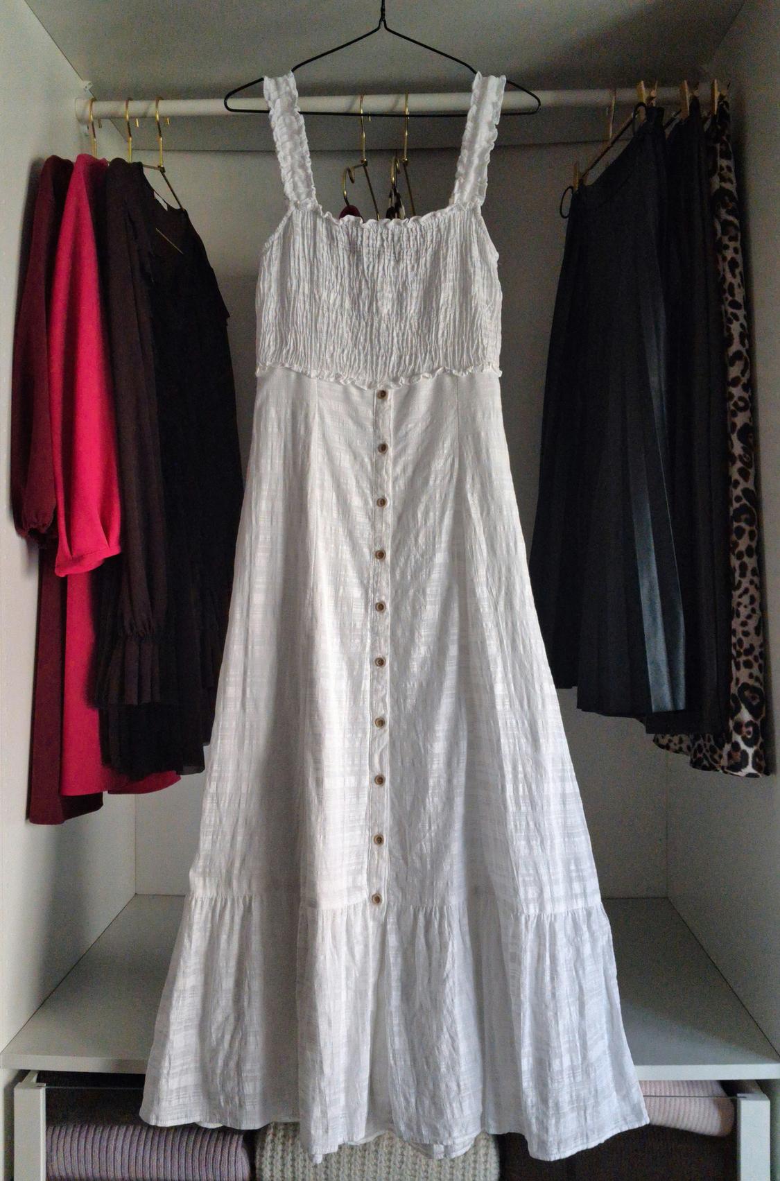 White dress with buttons hanging in a wardrobe, surrounded by dark-toned and leopard print garments.