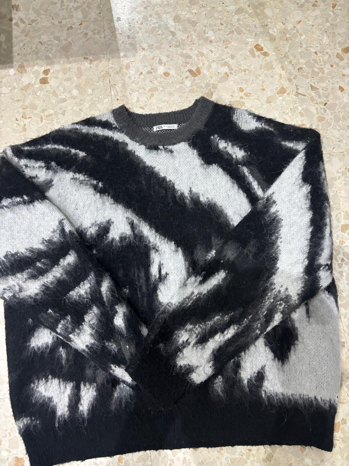 Wool jumper with abstract black and white pattern on a light tiled floor. Visible label on the collar.