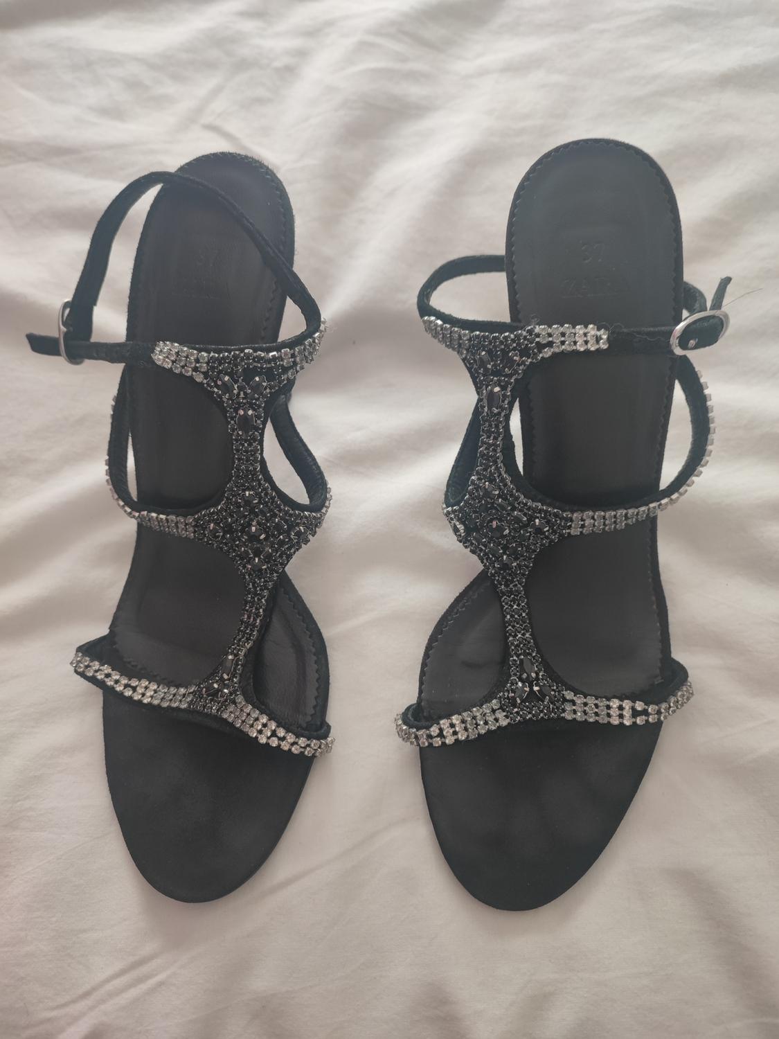 Black sandals with diamante-decorated straps on a white surface. Visible text: "37 ZARA".
