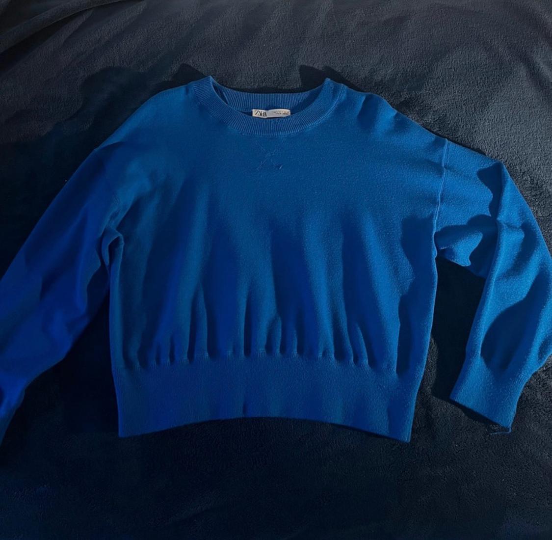 Long-sleeved blue jumper on a dark surface. The label in the neck says "Zara". The fabric has a soft finish.