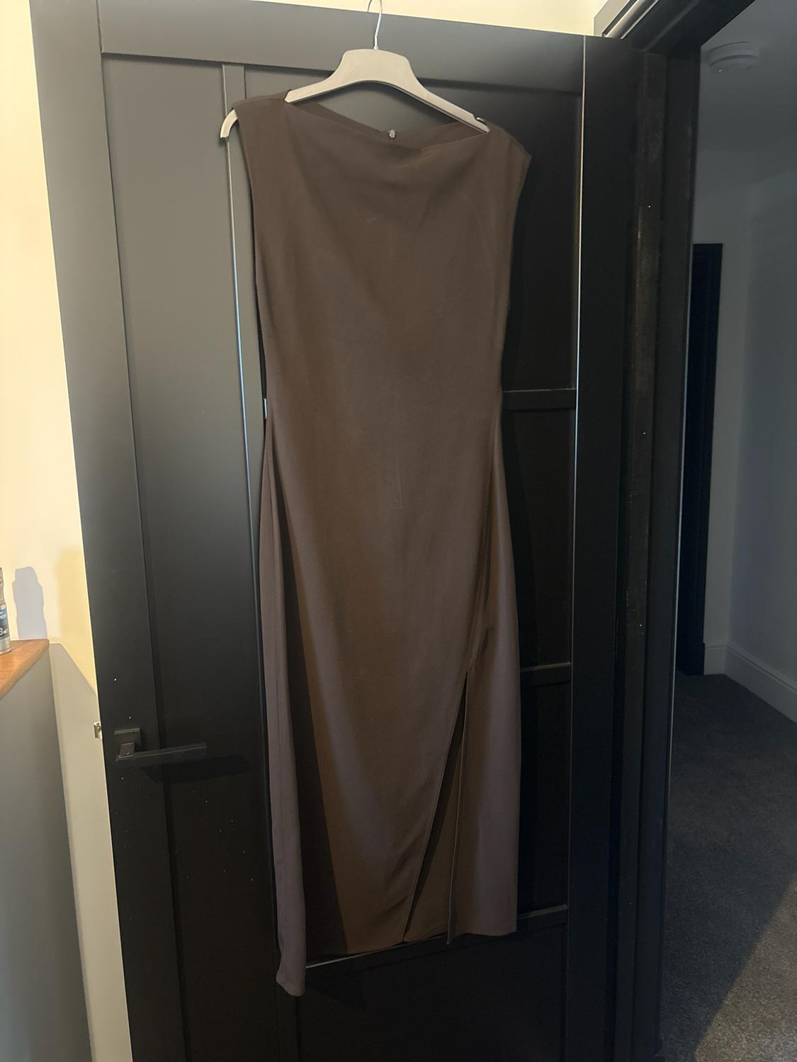 Dark brown sleeveless maxi dress with a side slit, hanging from a hanger on a black door indoors.