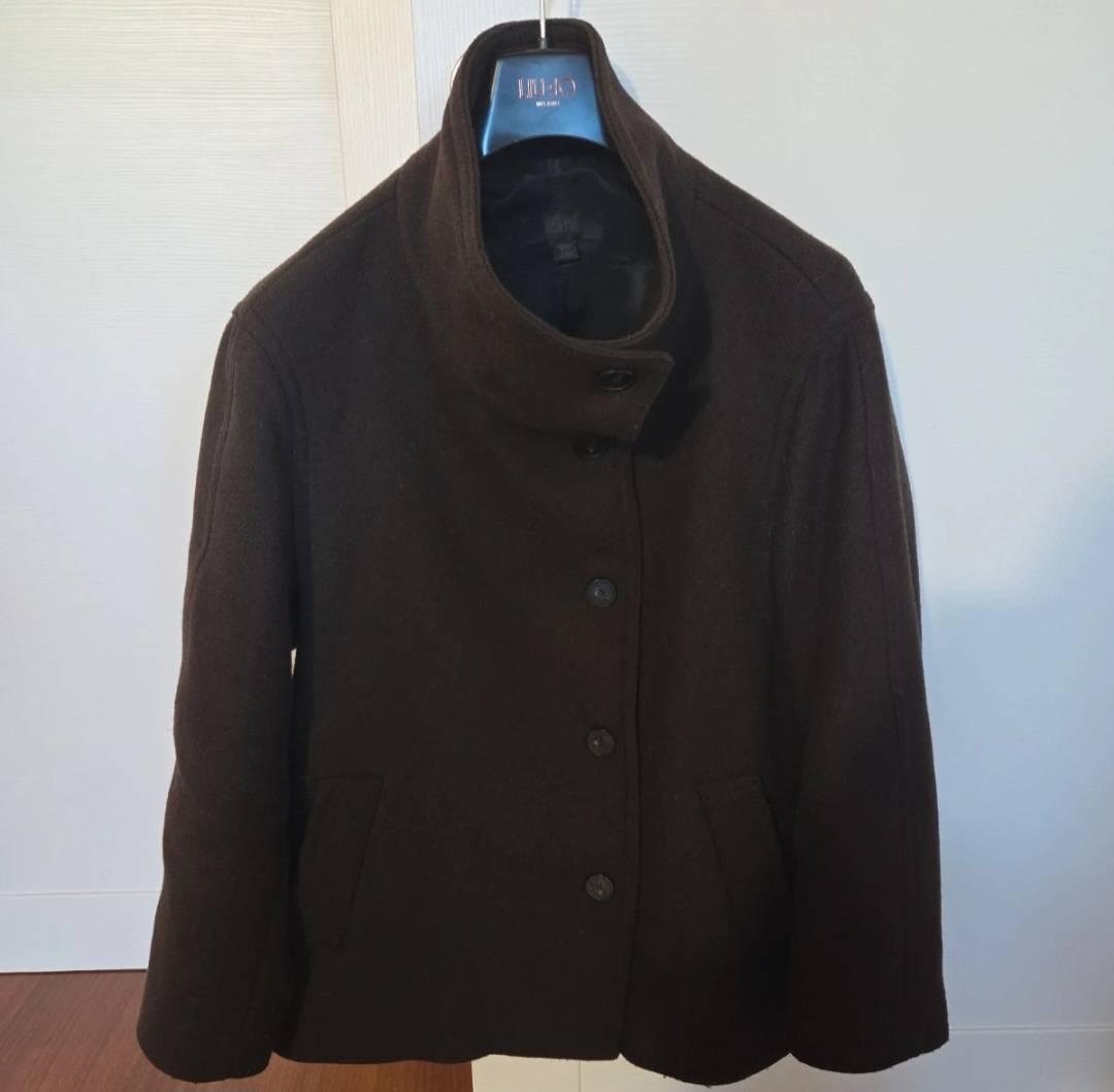 Dark brown coat with a high collar and front buttons, hanging on a blue hanger with the "JIL SANDER" brand. White background.