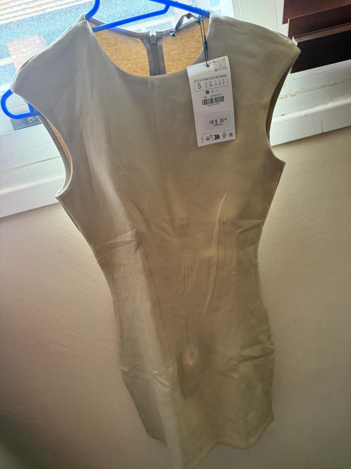 Beige sleeveless dress on a blue hanger in front of a window. Label with text S and US $35.90. Casual indoor setting.