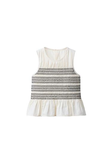 Front view of a sleeveless blouse with black embroidery and frill detailing on the hem.