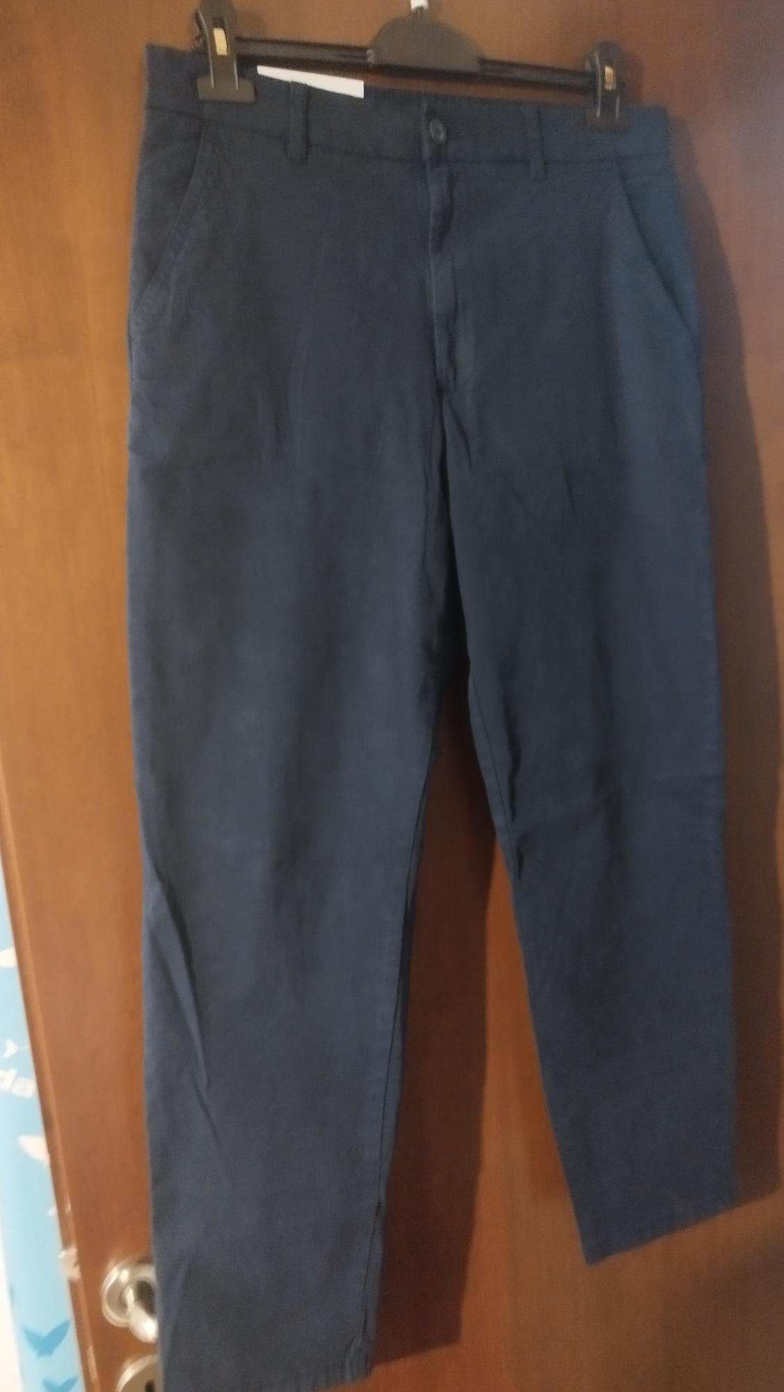 Dark blue trousers hanging on a hanger over a wooden door. The image shows details of pockets and front fastening.