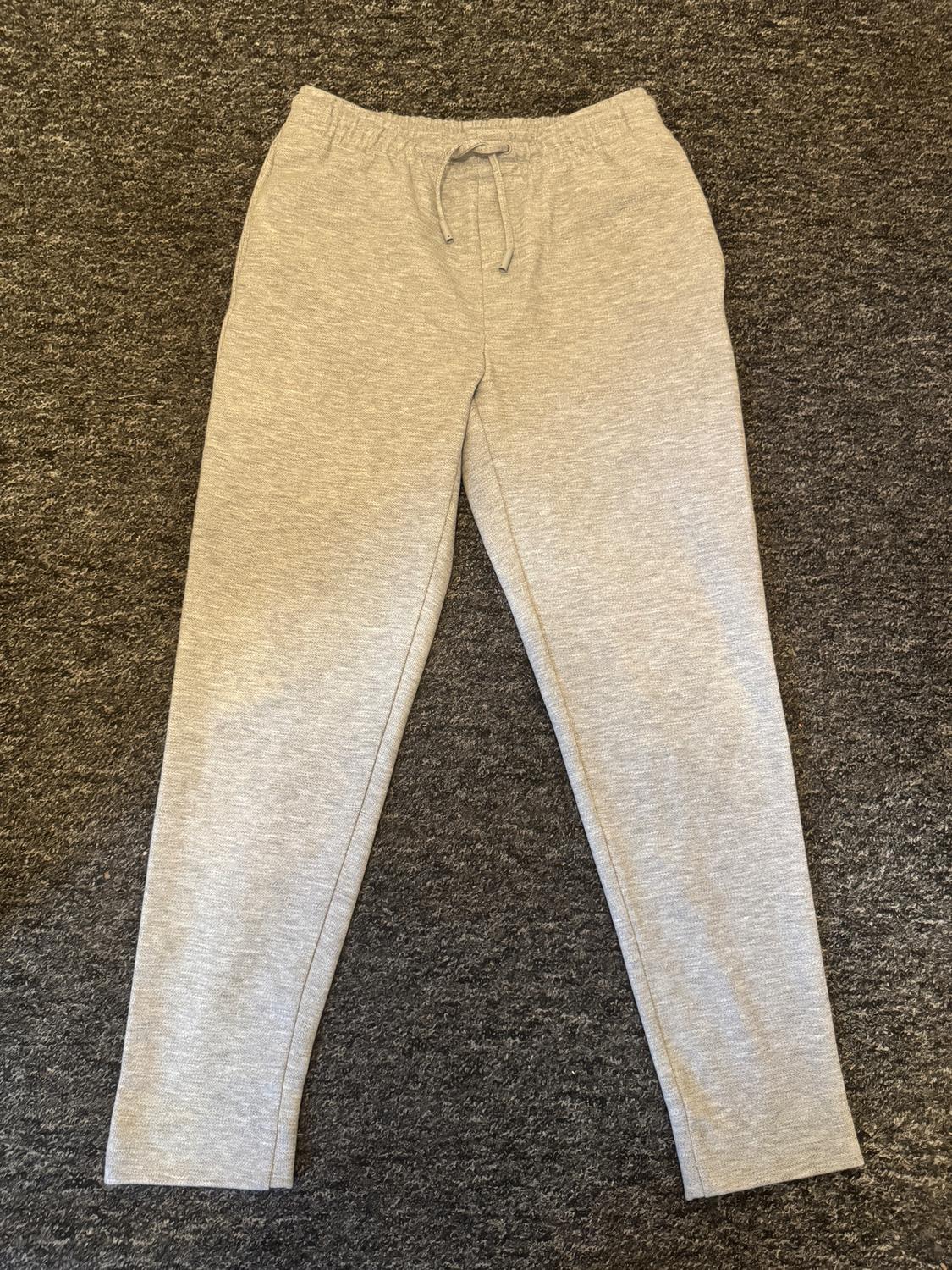 Grey jogging bottoms with an elasticated drawstring waist, placed on a grey rug.