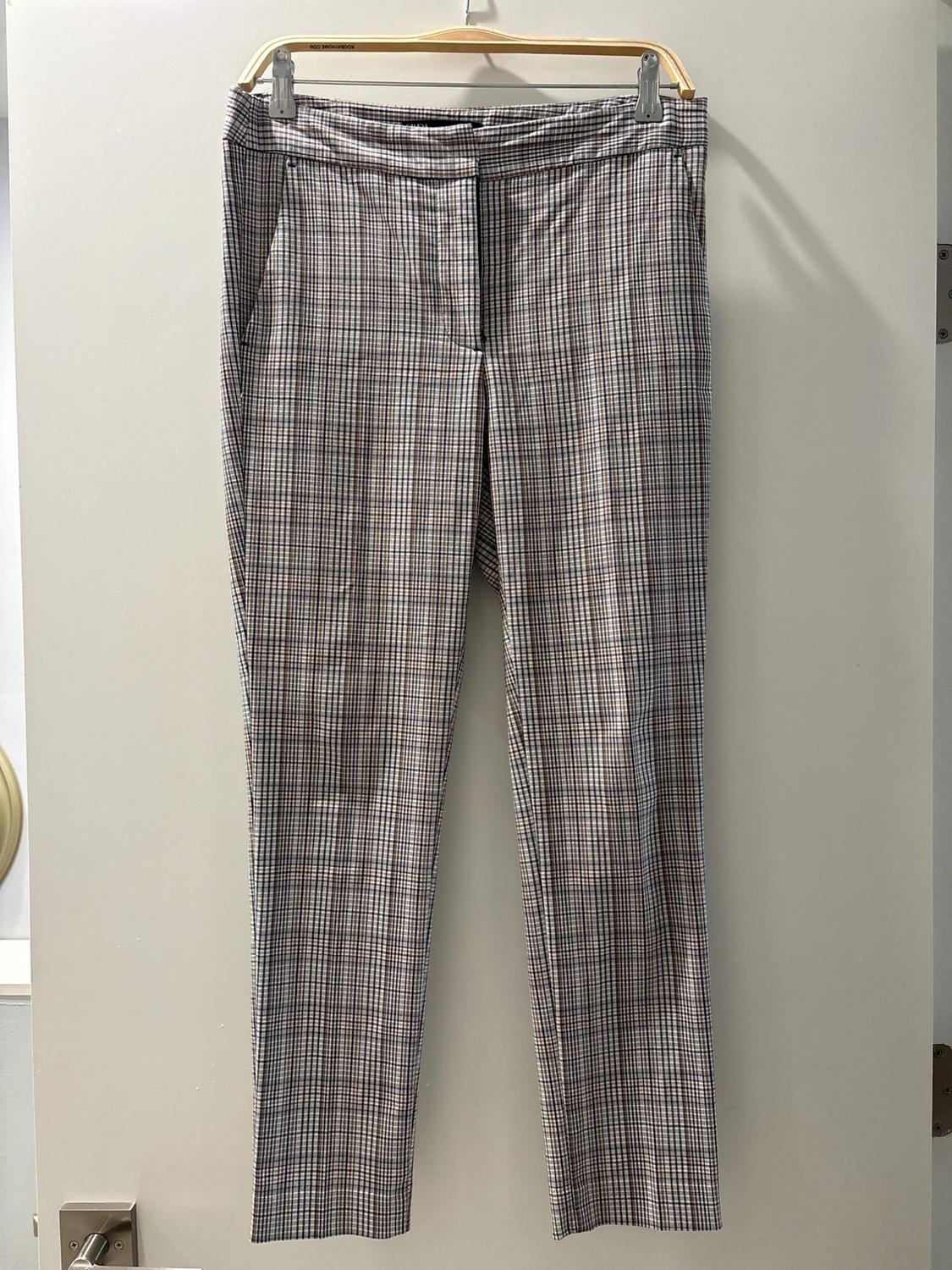 Plaid pants in shades of brown and white hanging on a wooden hanger over a white door.