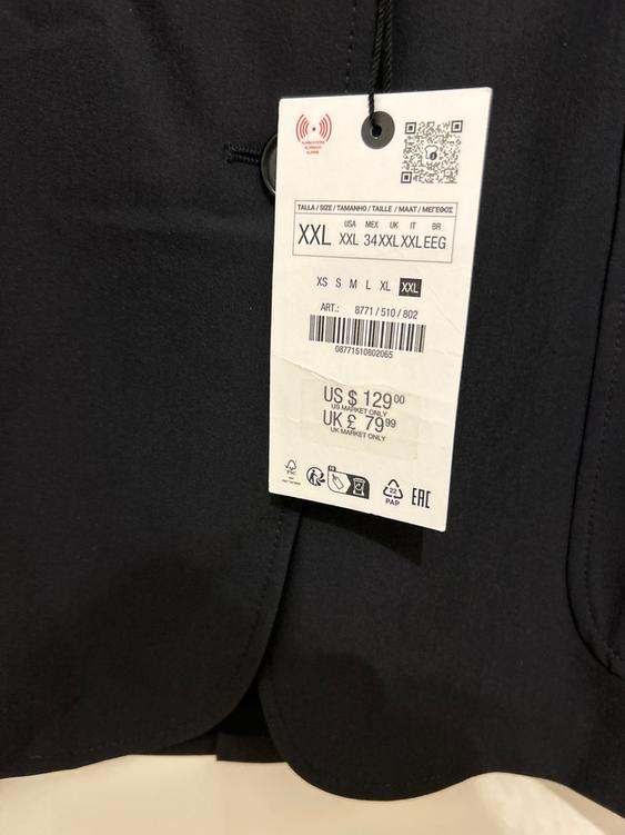 Black clothing label with XXL sizes and a price of $129 USD. Includes QR code and recycling symbols.