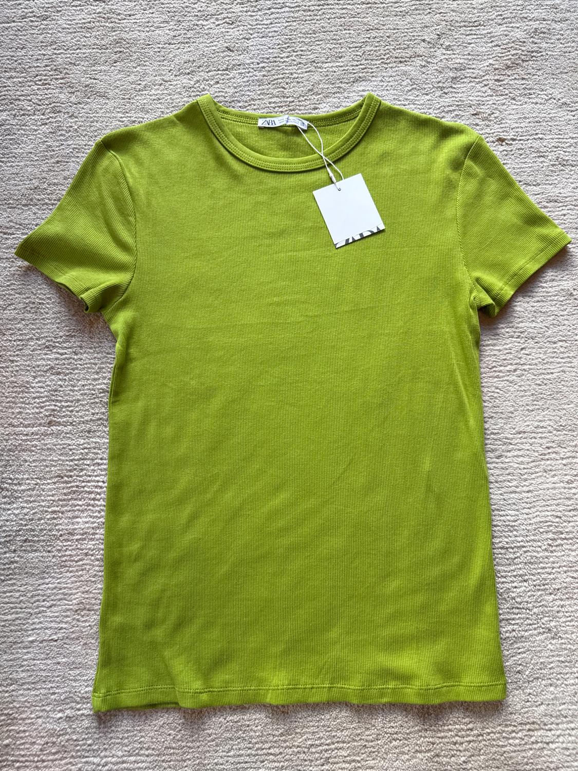 Lime green short-sleeved t-shirt on a beige rug, with a white hang tag.