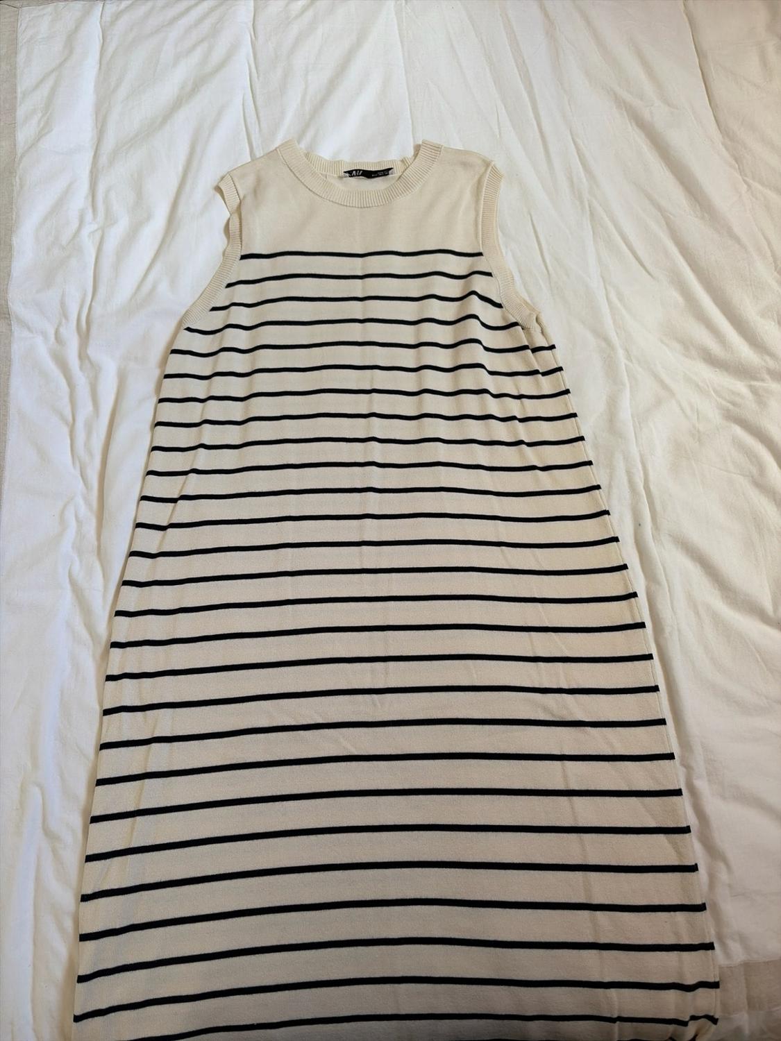 Cream-coloured sleeveless knit dress with horizontal black stripes, laid out on a white sheet.