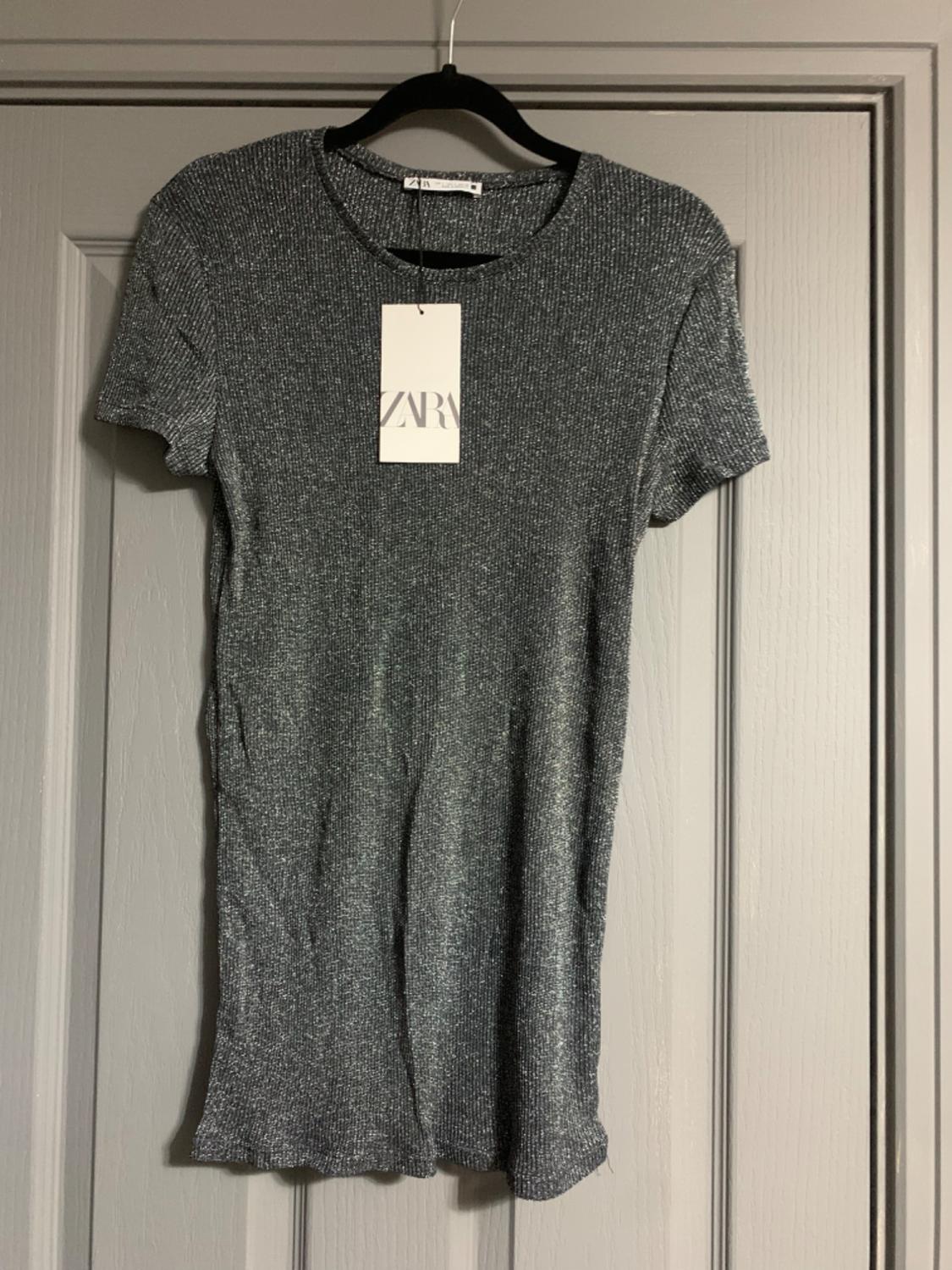 Grey knitted dress hanging on a black hanger over a grey door. Visible label with the text "ZARA".