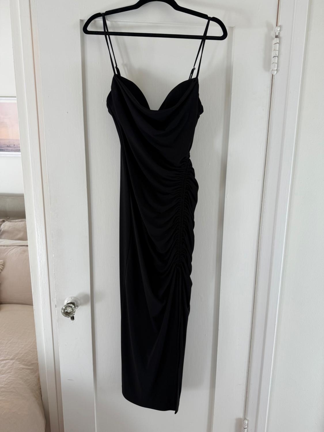 Front view of a black dress with thin straps and a side ruching detail. Knee-length.