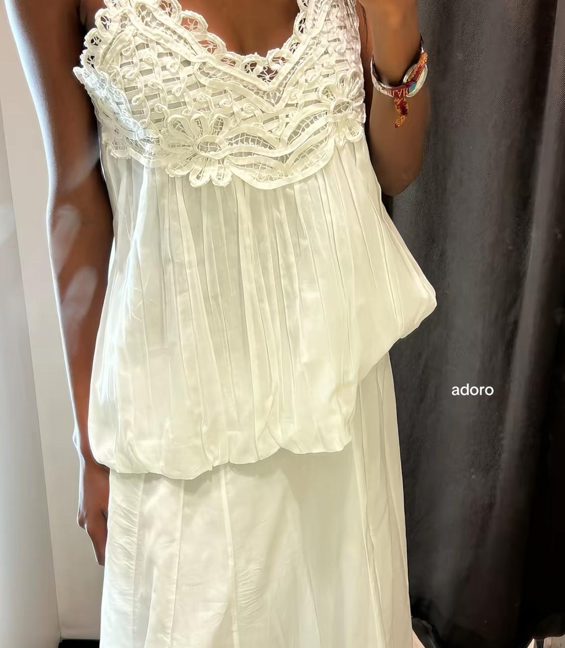 Model wearing a white pleated top with lace detailing, paired with a white skirt. Relaxed style. Text in the image: adore.