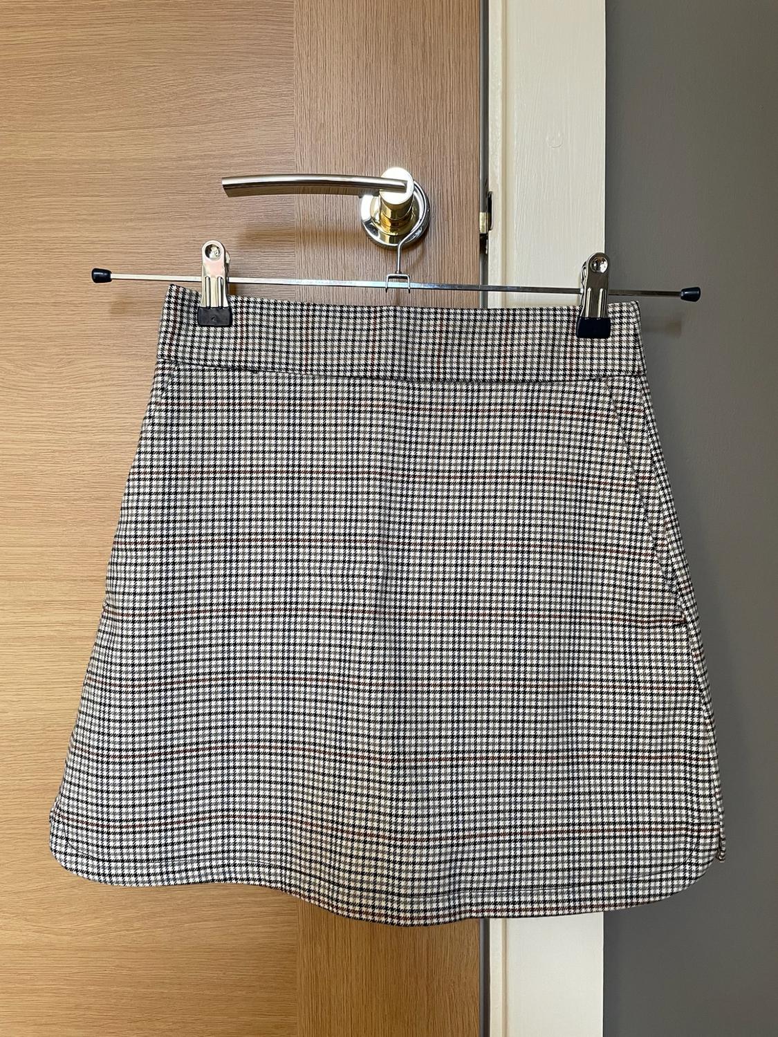 Short plaid skirt hanging from a metal hanger on the silver knob of a wooden door.