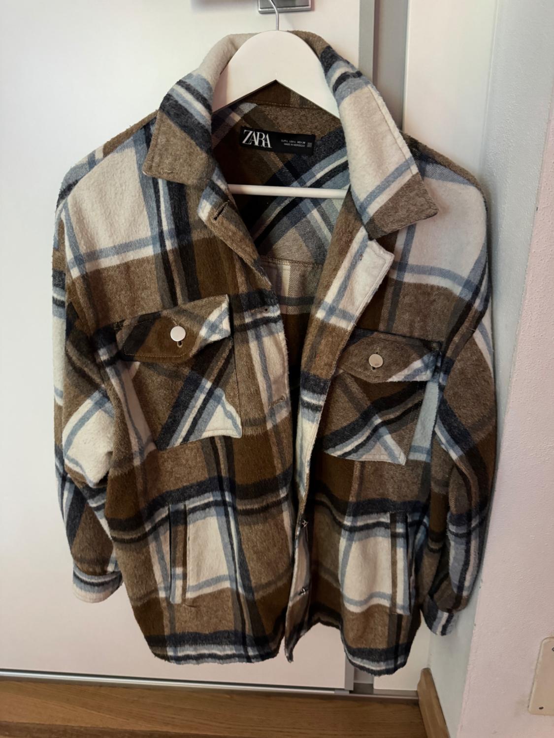 Brown, white, and blue checked jacket hanging on a white hanger. Visible label: "ZARA".