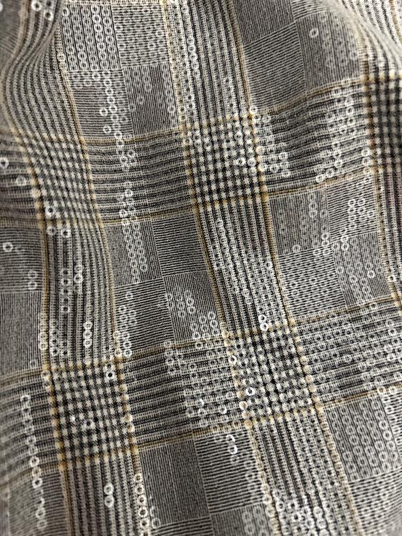 Fabric with a checked pattern in grey and beige tones, decorated with shimmering sequins that reflect the light.