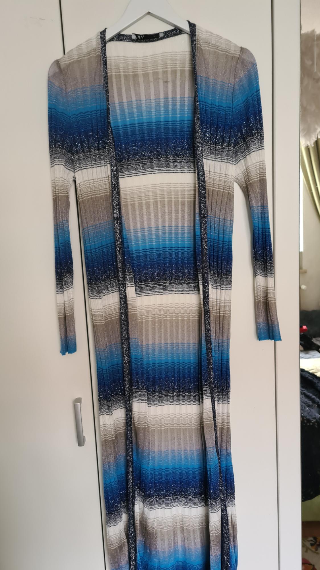 A long dress with horizontal stripes in shades of blue, grey, and white, hanging on a white hanger in front of a white wardrobe.