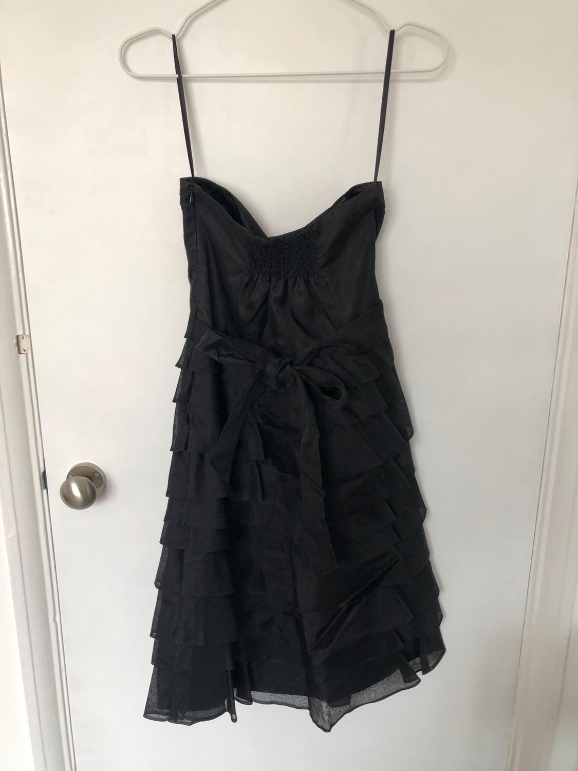 Front view of black dress with thin straps, layered ruffles and bow at the waist.
