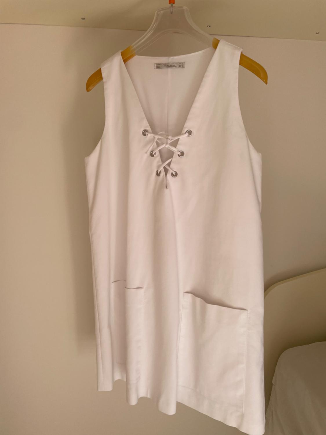 Front view of a white dress with a V-neck, criss-cross lacing, and front pockets.
