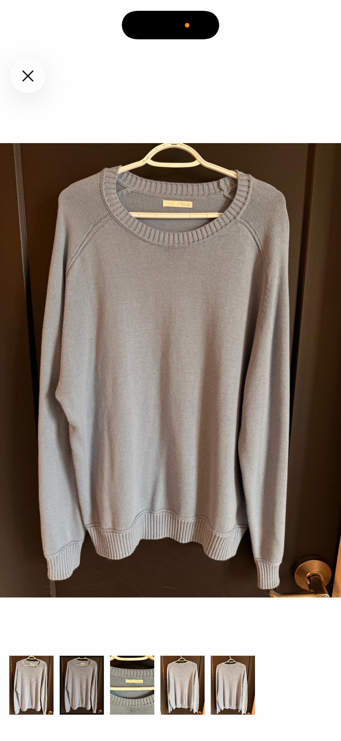 Light blue crew neck long-sleeve knit sweater, hanging on a white hanger on a brown door.