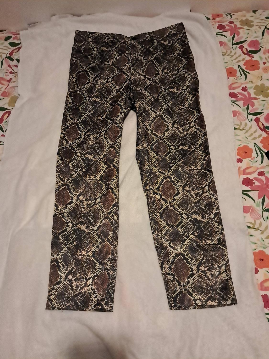 Trousers with a snake-print pattern in shades of brown, laid out on a white surface with a floral fabric background.