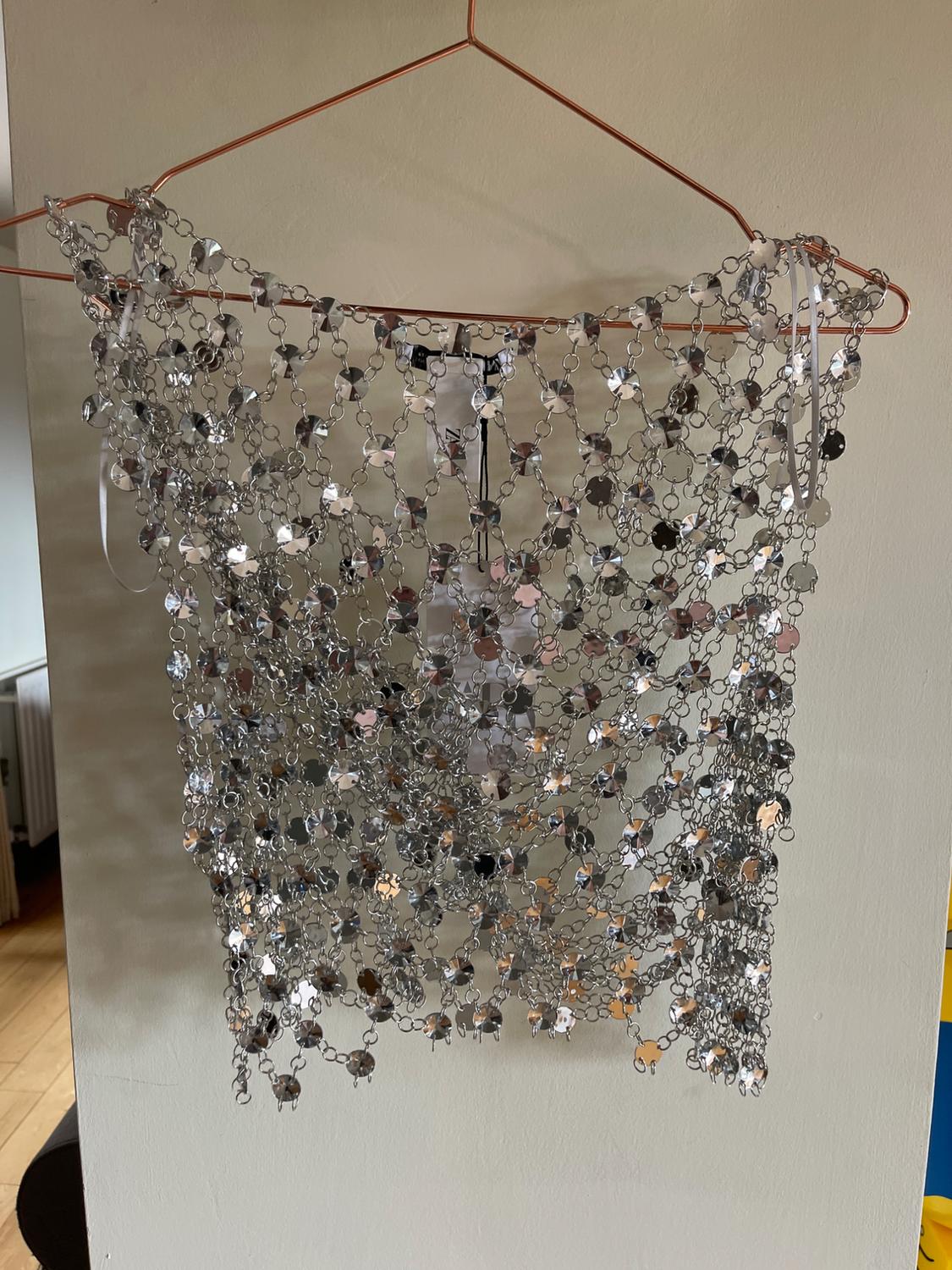 Silver-coloured metal mesh top with sparkly detailing, hanging on a copper wire hanger in front of a white wall.