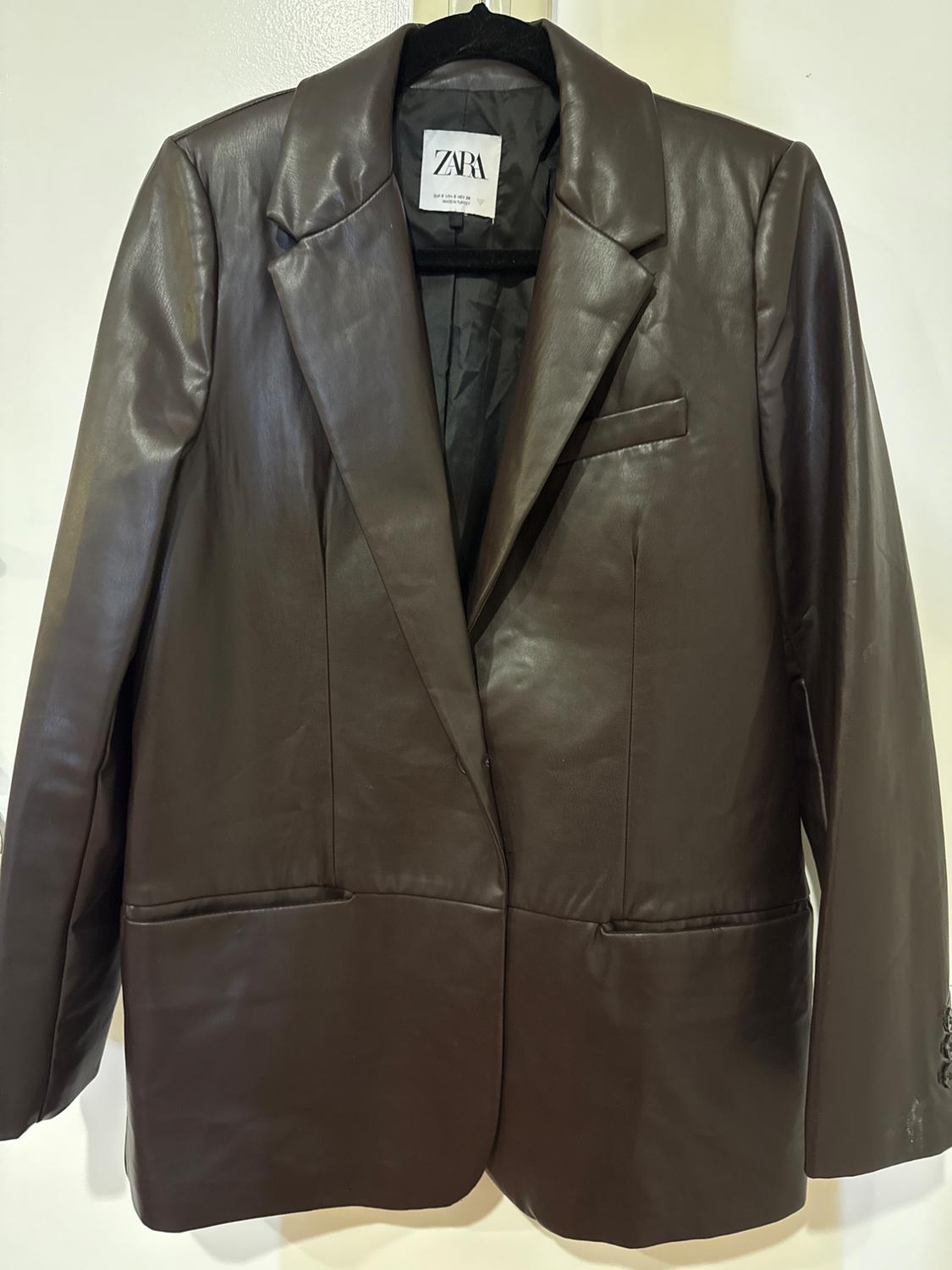 Brown leather jacket hanging on a black hanger. Visible label with the text "ZARA". White background.