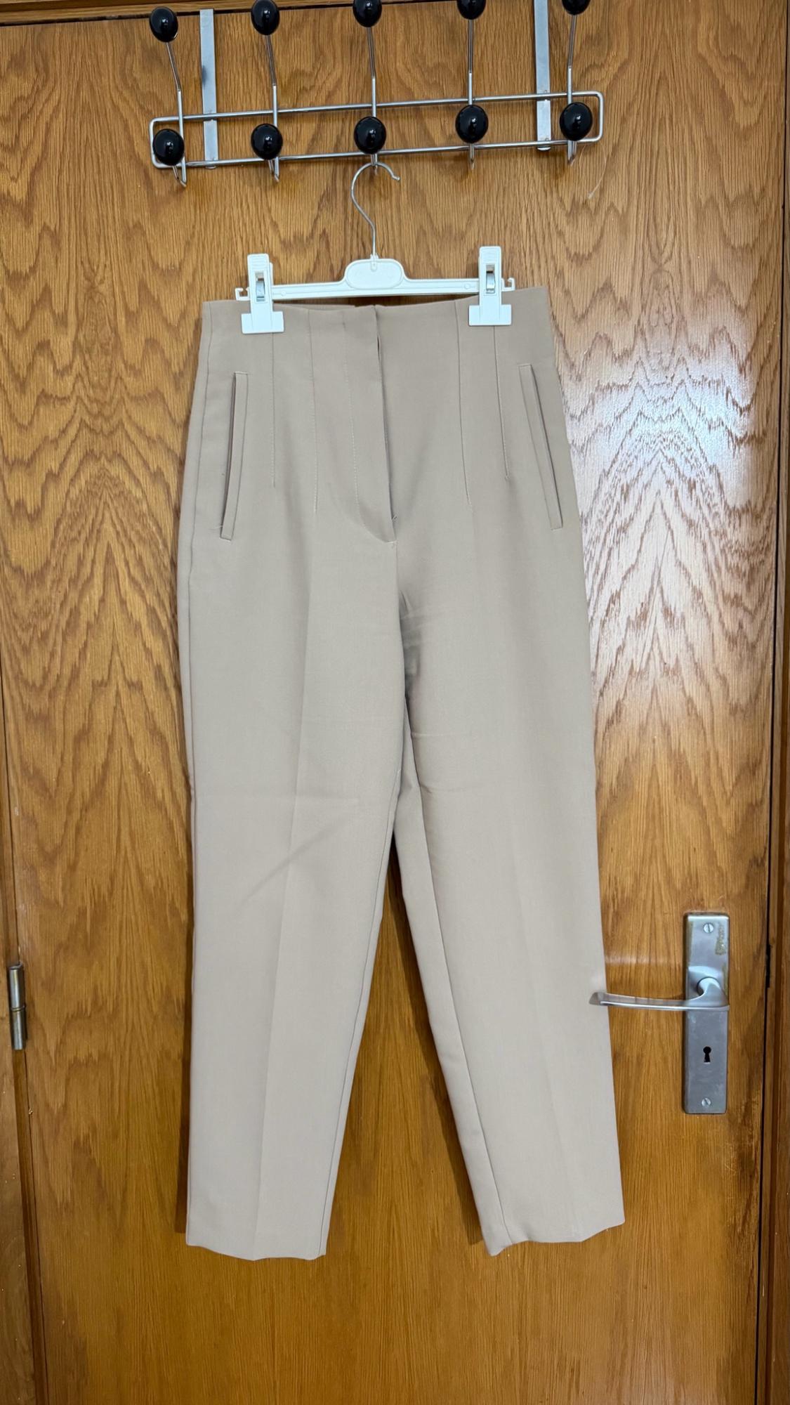 Beige trousers hanging on a white hanger on a wooden door with a metal coat rack.