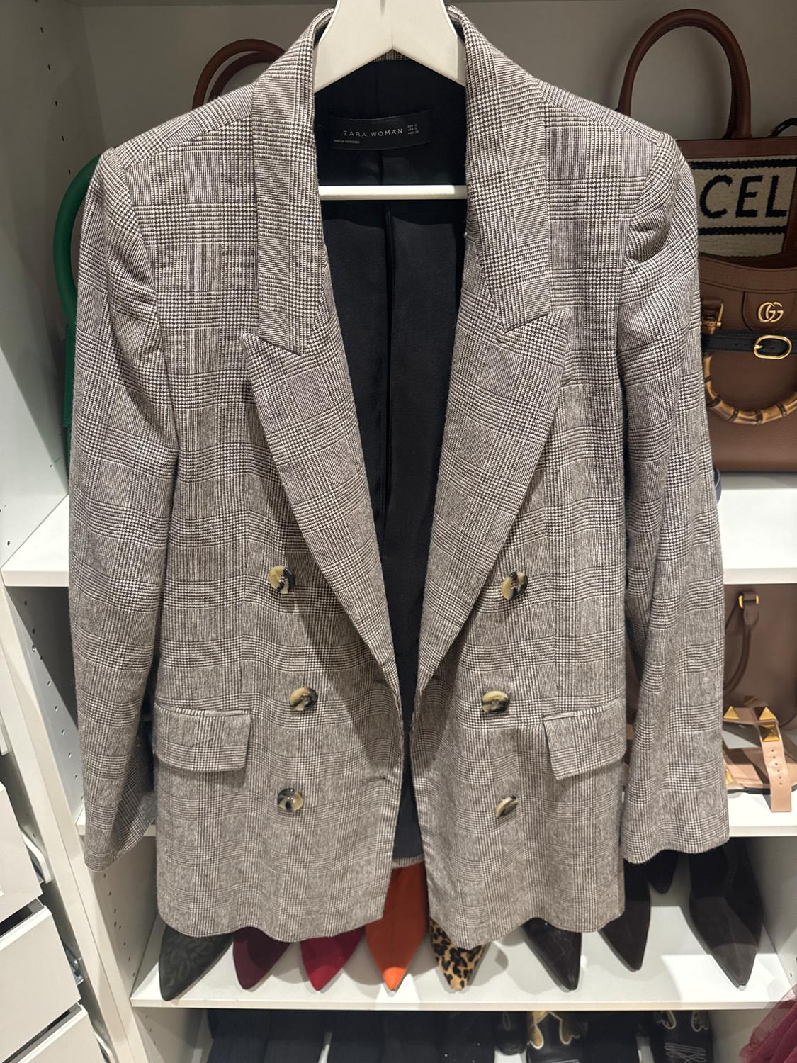 Grey double-breasted checked blazer hanging on a rack, surrounded by handbags and shoes in a white wardrobe.