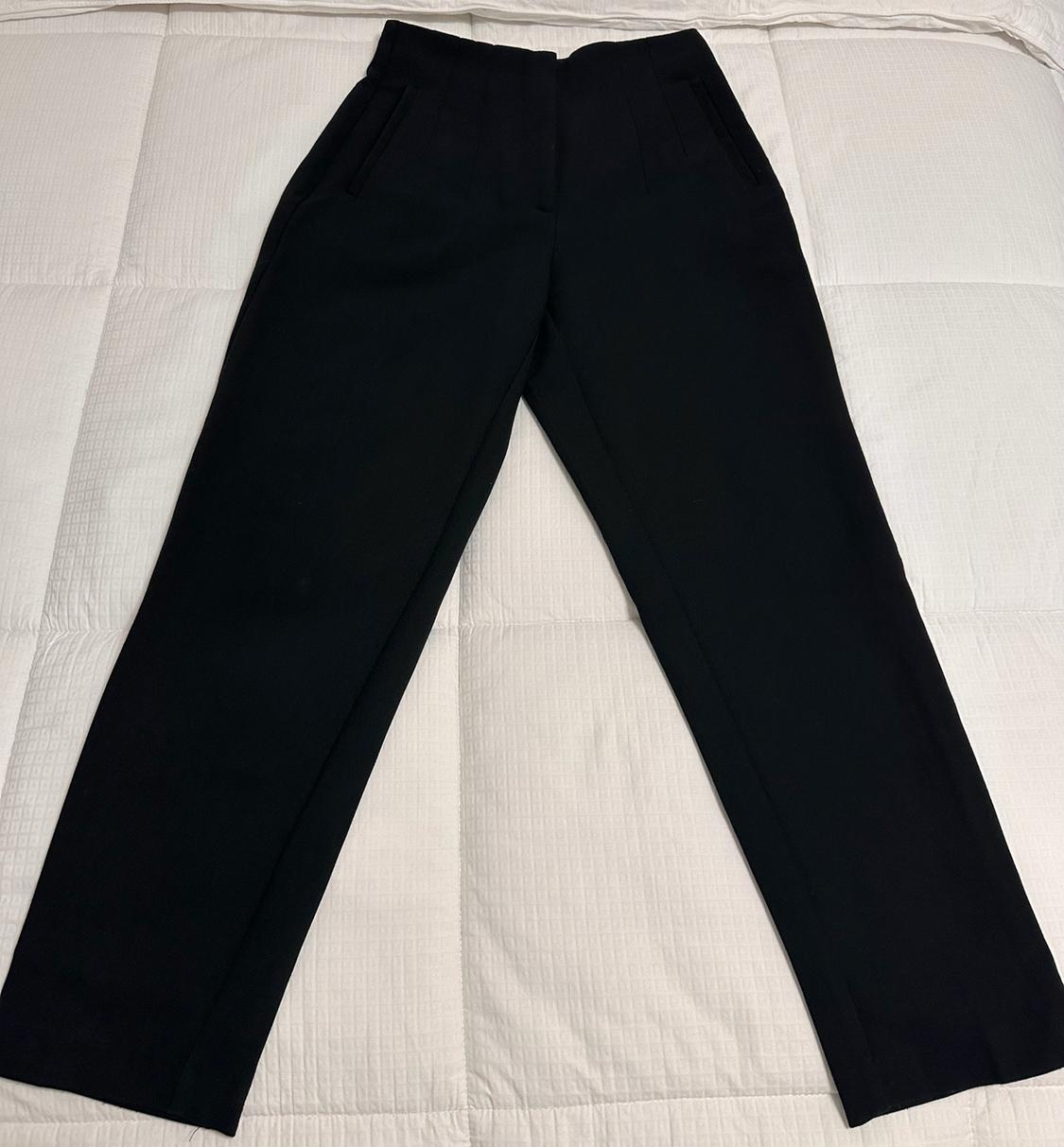Black pleated pants with side pockets, on a padded white surface.