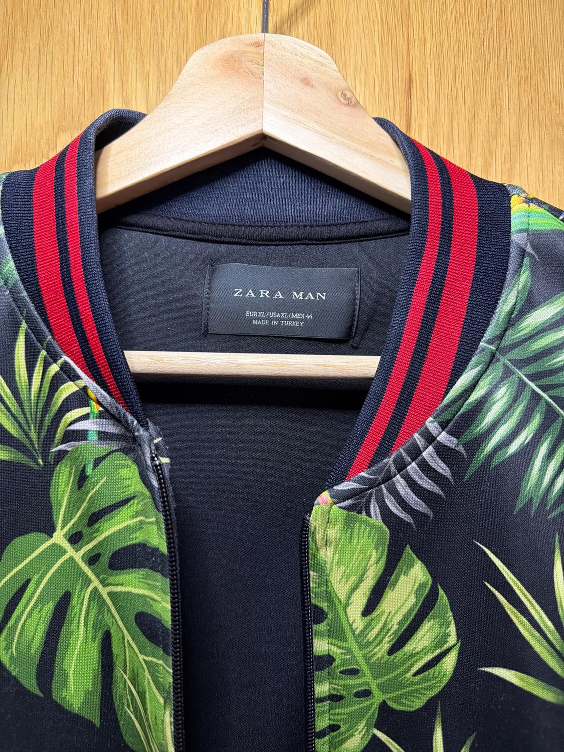 Jacket with green leaf print and red and black striped collar, hanging on a wooden hanger. Label: ZARA MAN.