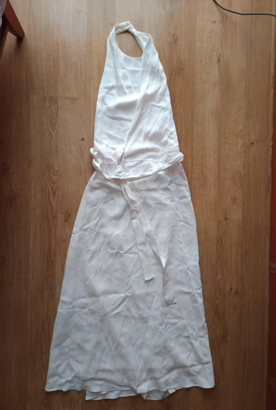 Long white halterneck dress with a bow detail at the waist, laid out on a wooden floor.