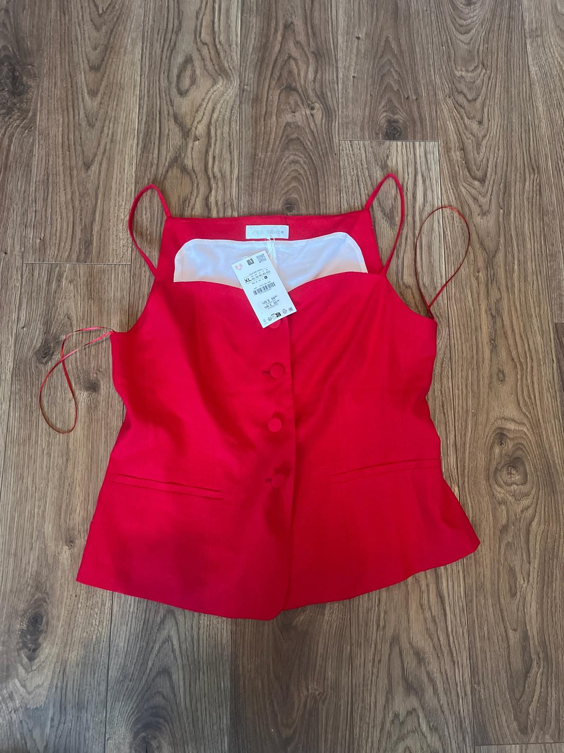Red camisole top with front buttons and a ZARA XL label, on a wooden floor.