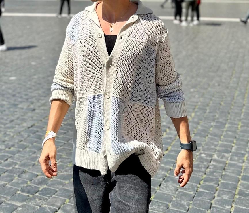Person in a beige knitted cardigan and black T-shirt, walking on cobblestones. Wearing a watch and bracelet on their left wrist.