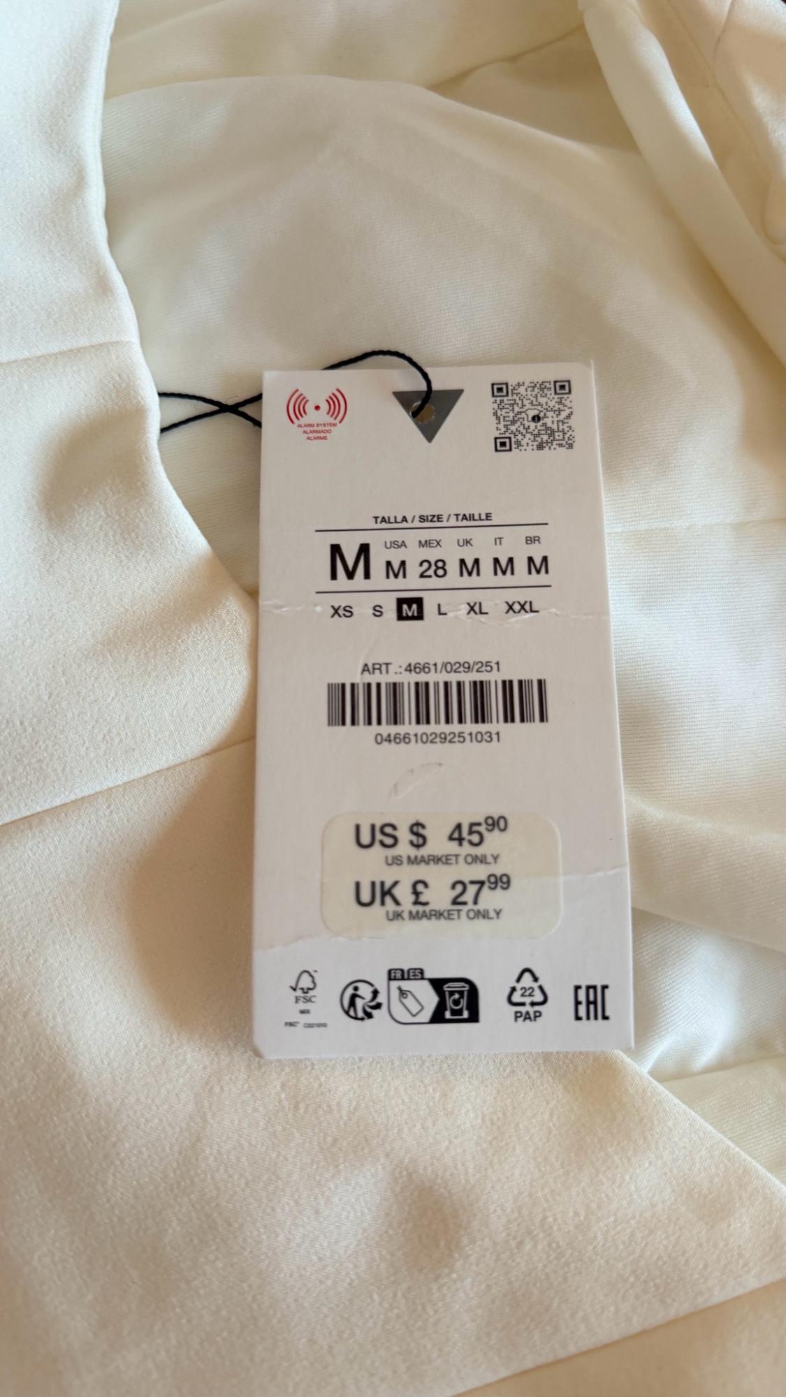 White garment with label and QR code. Text: TALLA / SIZE / TAILLE M, ART.: 4661/029/251, US $ 45.90 US MARKET ONLY, UK £ 27.99.