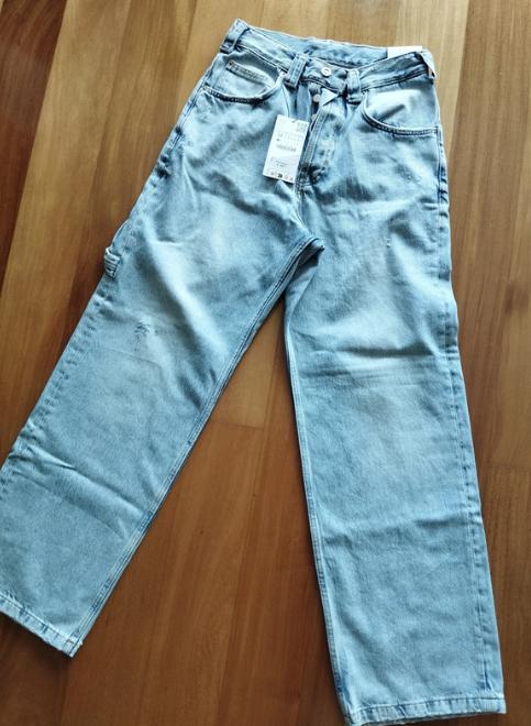 Wide-leg blue jeans on a wooden floor, with a white tag hanging from the waistband.