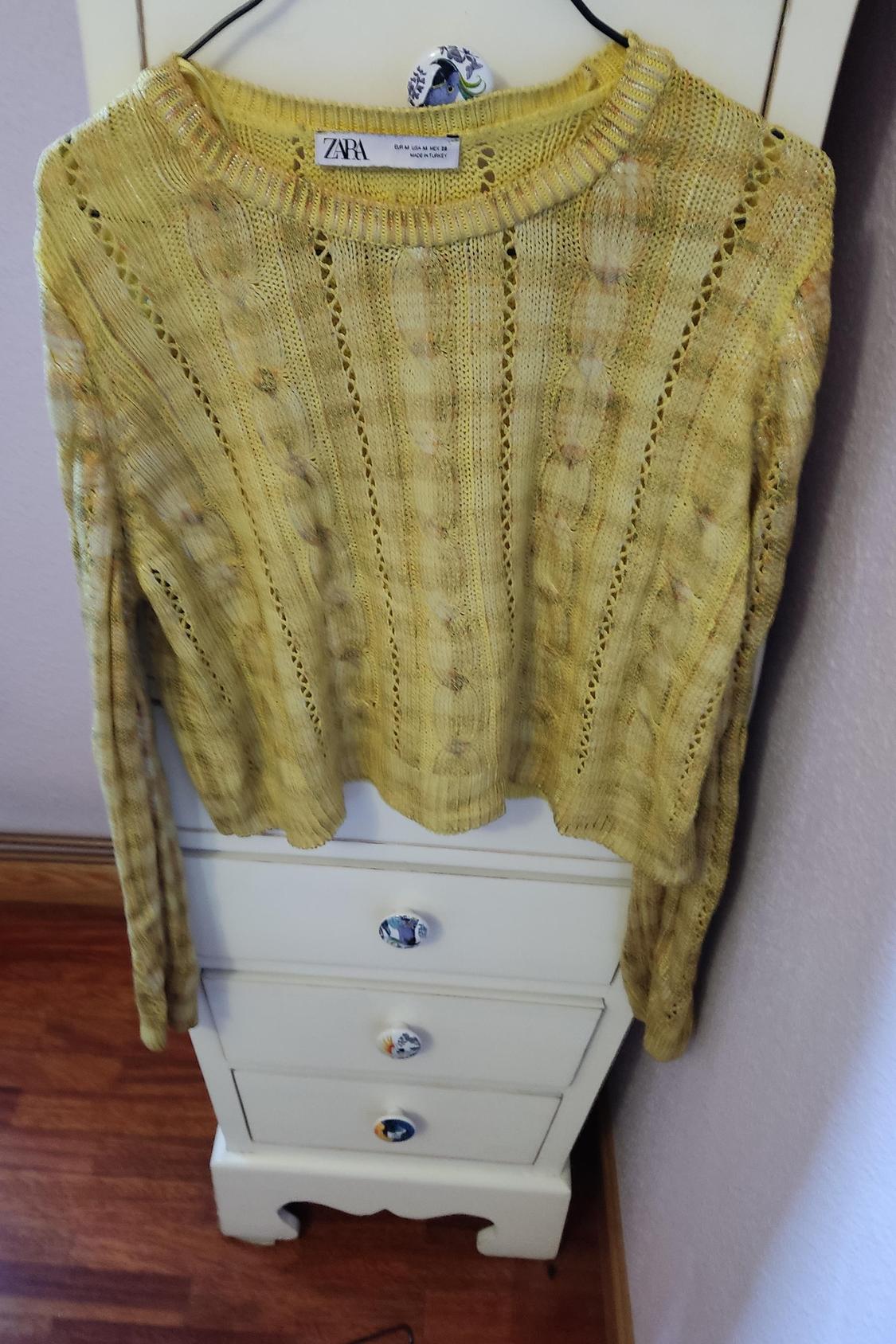 Front view of a yellow jumper with a cable knit pattern hanging on a hanger.