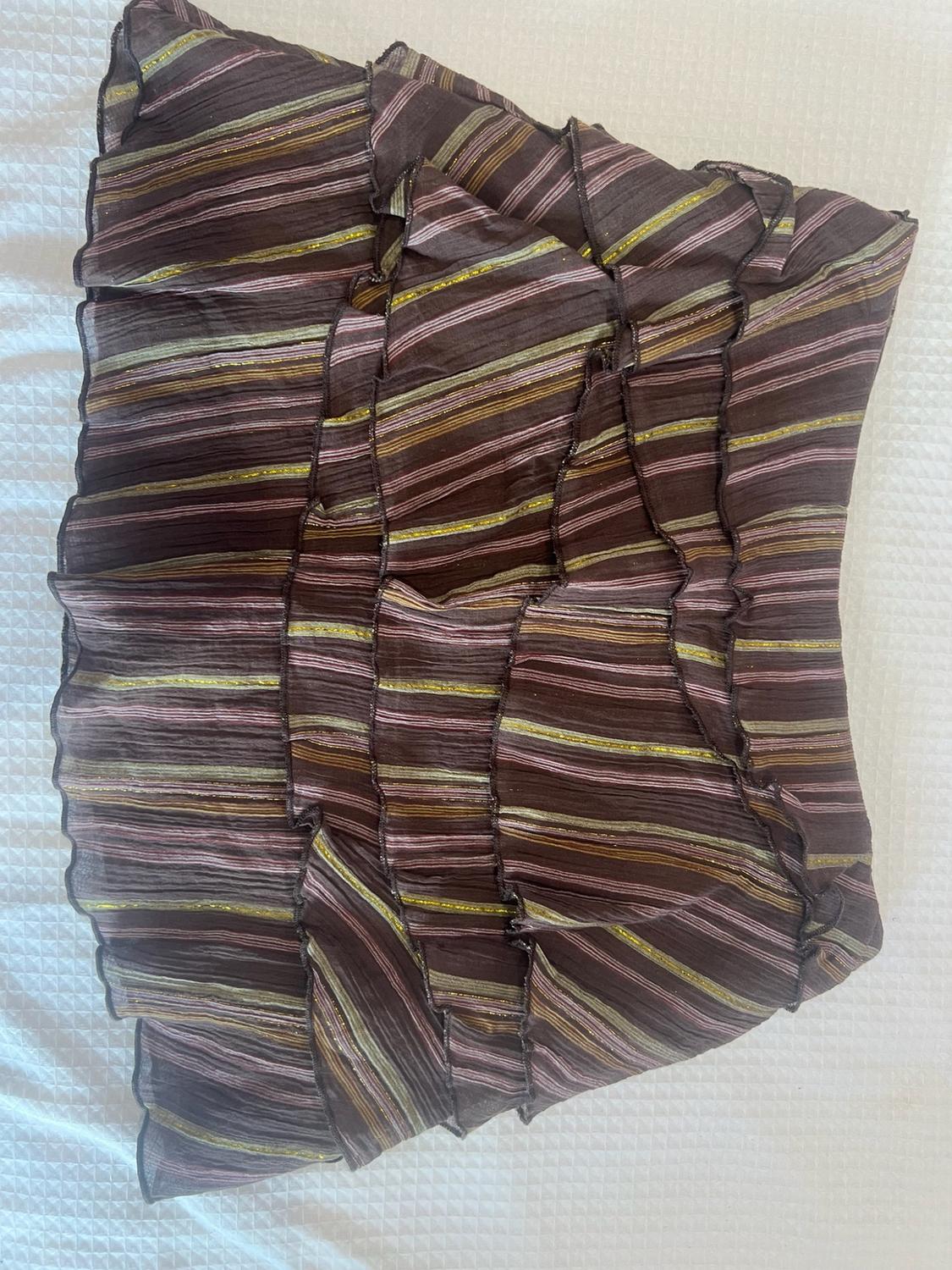 Brown skirt with horizontal pink and gold stripes and ruffle details, on a textured white surface.